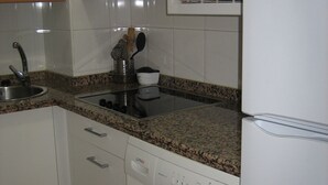 Cocina compacta con alacenas blancas, microondas integrado, un lavamanos y lavadora de carga frontal.
