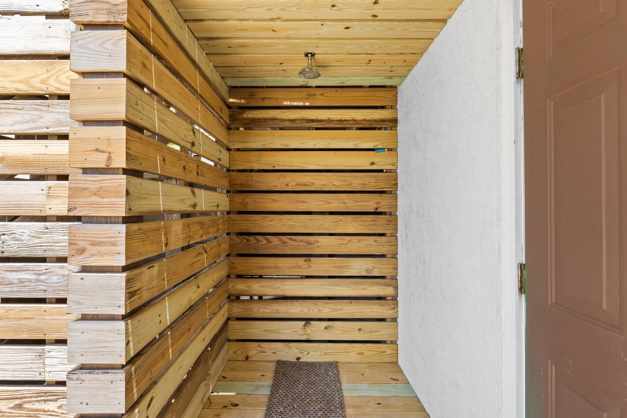 A narrow wooden hallway with a ceiling fan, a door on the right, and a wooden wall on the left.