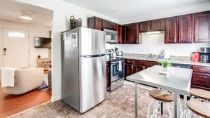 A modern kitchen with stainless steel appliances, dark wooden cabinets, and a tiled floor.
