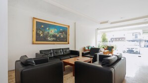 A modern living room with black leather sofas, a wooden coffee table, and a large framed painting on the wall. - Istana Permata Ngagel (Surabaya)