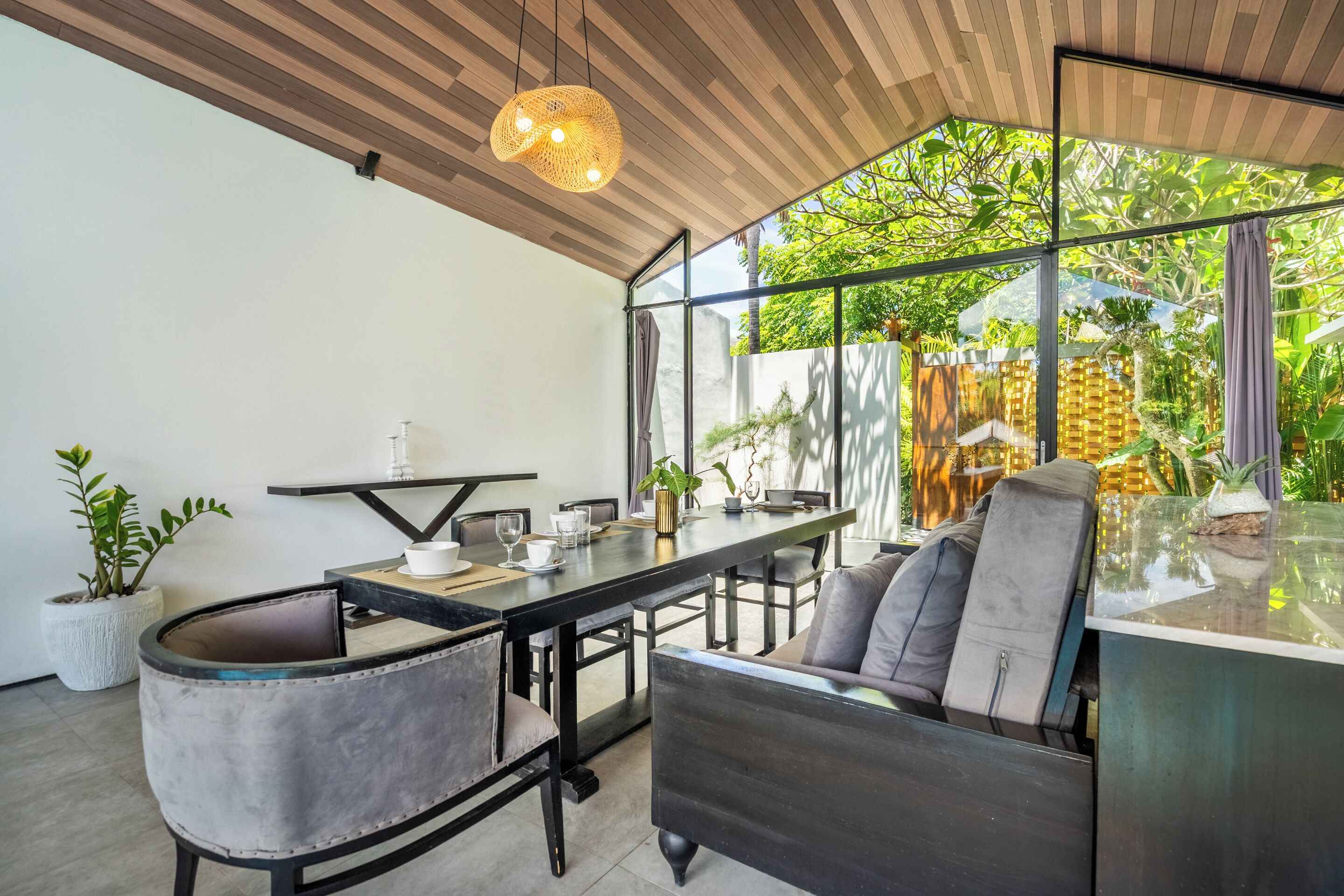 Un comedor moderno con una mesa de vidrio, sillas acolchadas y una lámpara colgante.