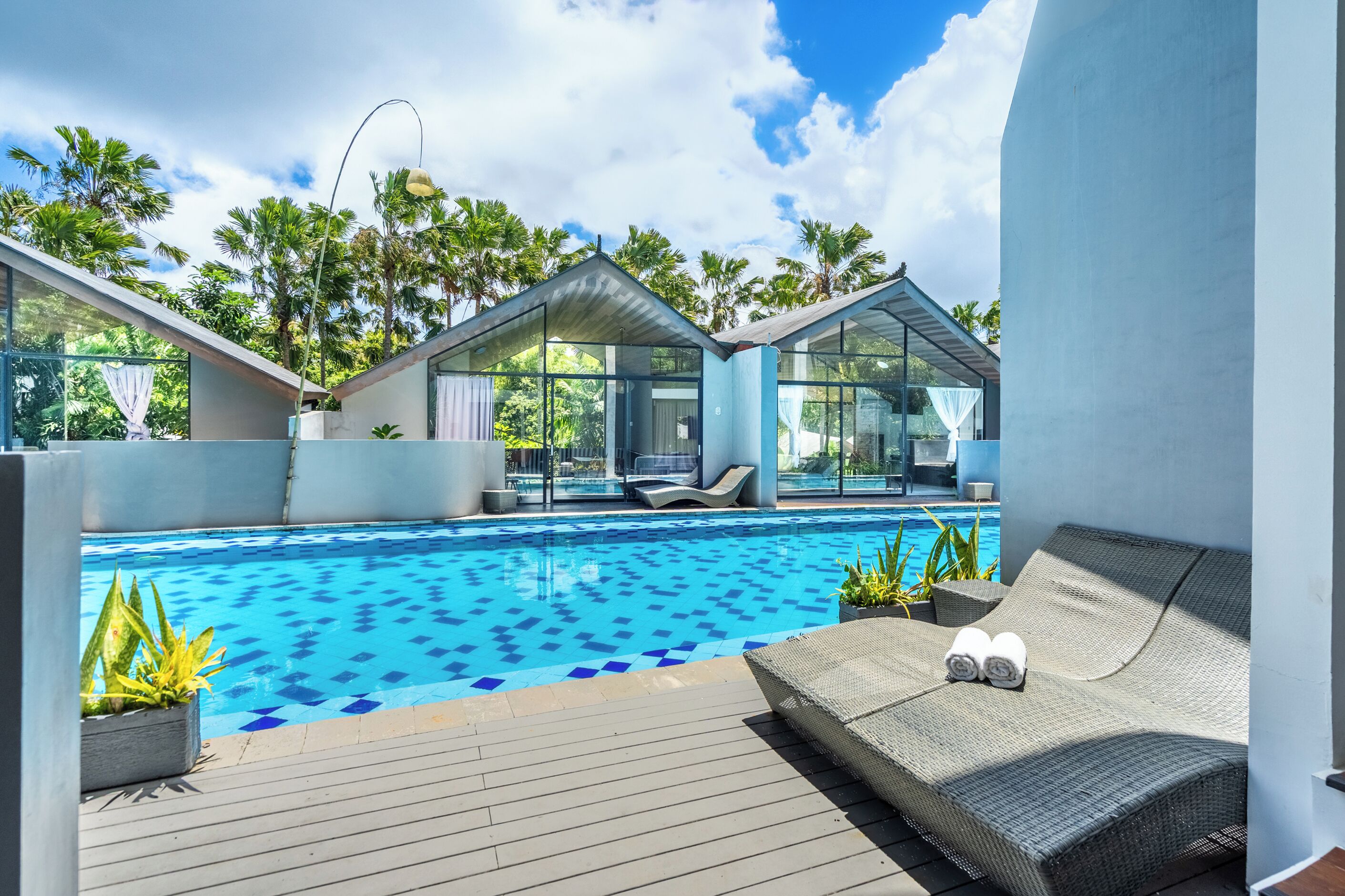 Un área de piscina moderna con sillones de descanso y una estructura de cristal.
