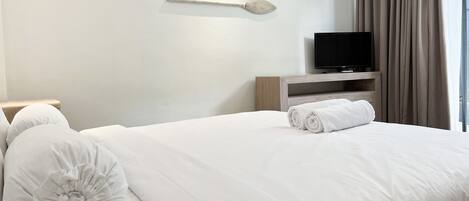 A neatly made bed with white bedding and pillows, a television on a wooden stand, and a wall-mounted air conditioner.