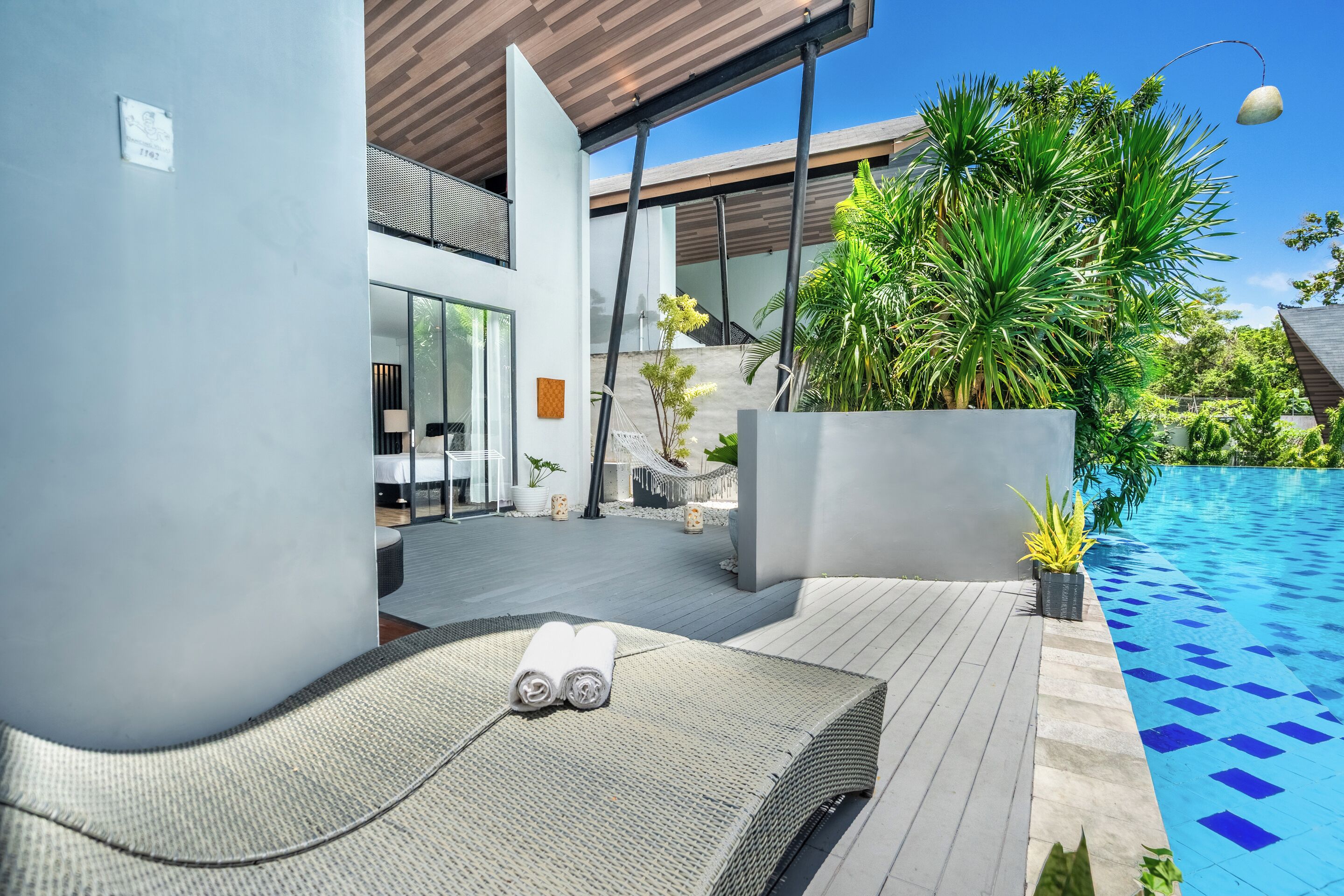 Un espace de détente extérieur moderne, doté d’une piscine, de chaises longues et de plantes en pot.