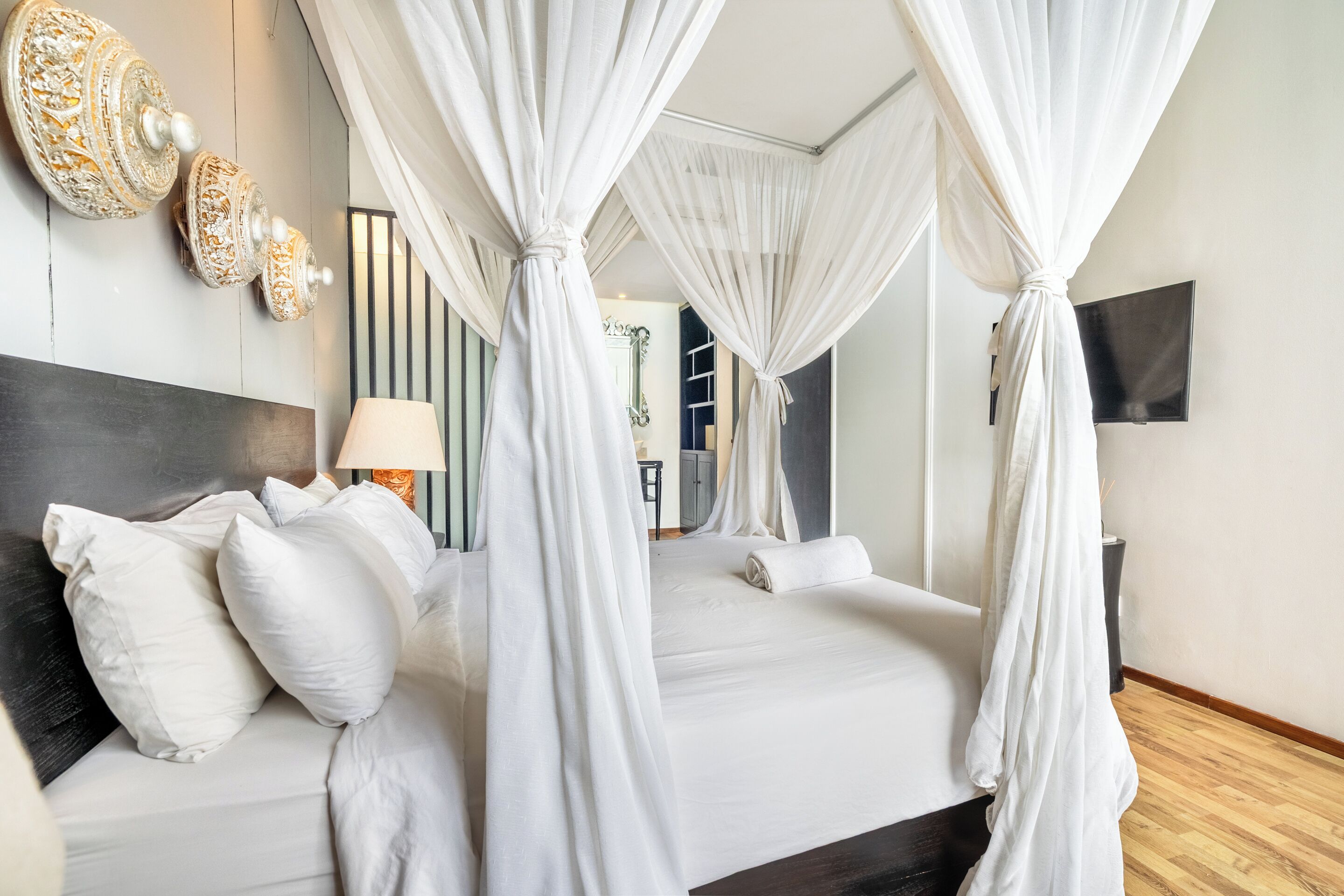 A bedroom with a four-poster bed, a bedside lamp, and a flat-screen TV on the wall.
