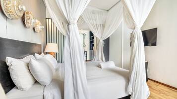 A bedroom with a four-poster bed, a bedside lamp, and a flat-screen TV on the wall.
