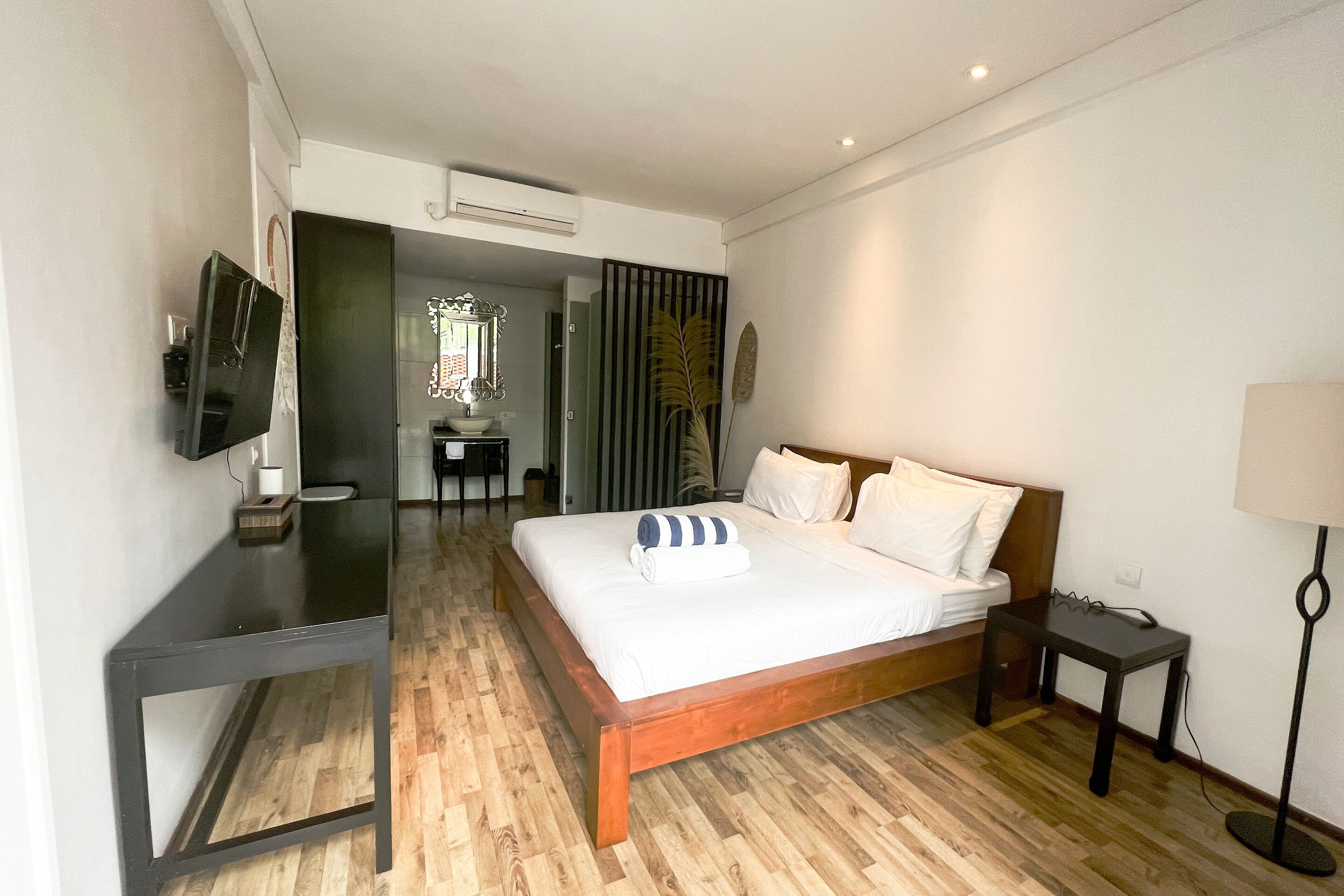 A hotel room with a wooden bed, a desk, a chair, a TV, and a lamp.