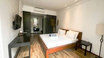 A hotel room with a wooden bed, a desk, a chair, a TV, and a lamp.