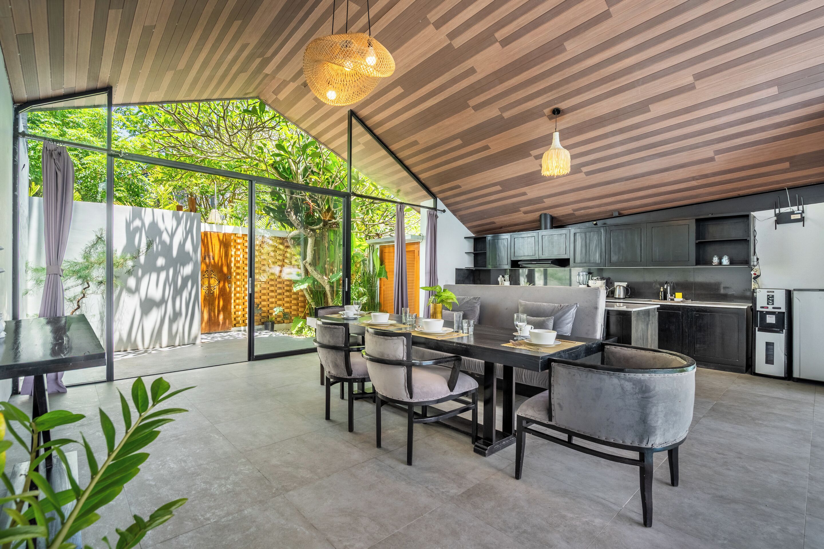 Una cucina moderna con mobili scuri, un'area pranzo con tavolo e sedie, e un'ampia porta-vetro che dà su un giardino.