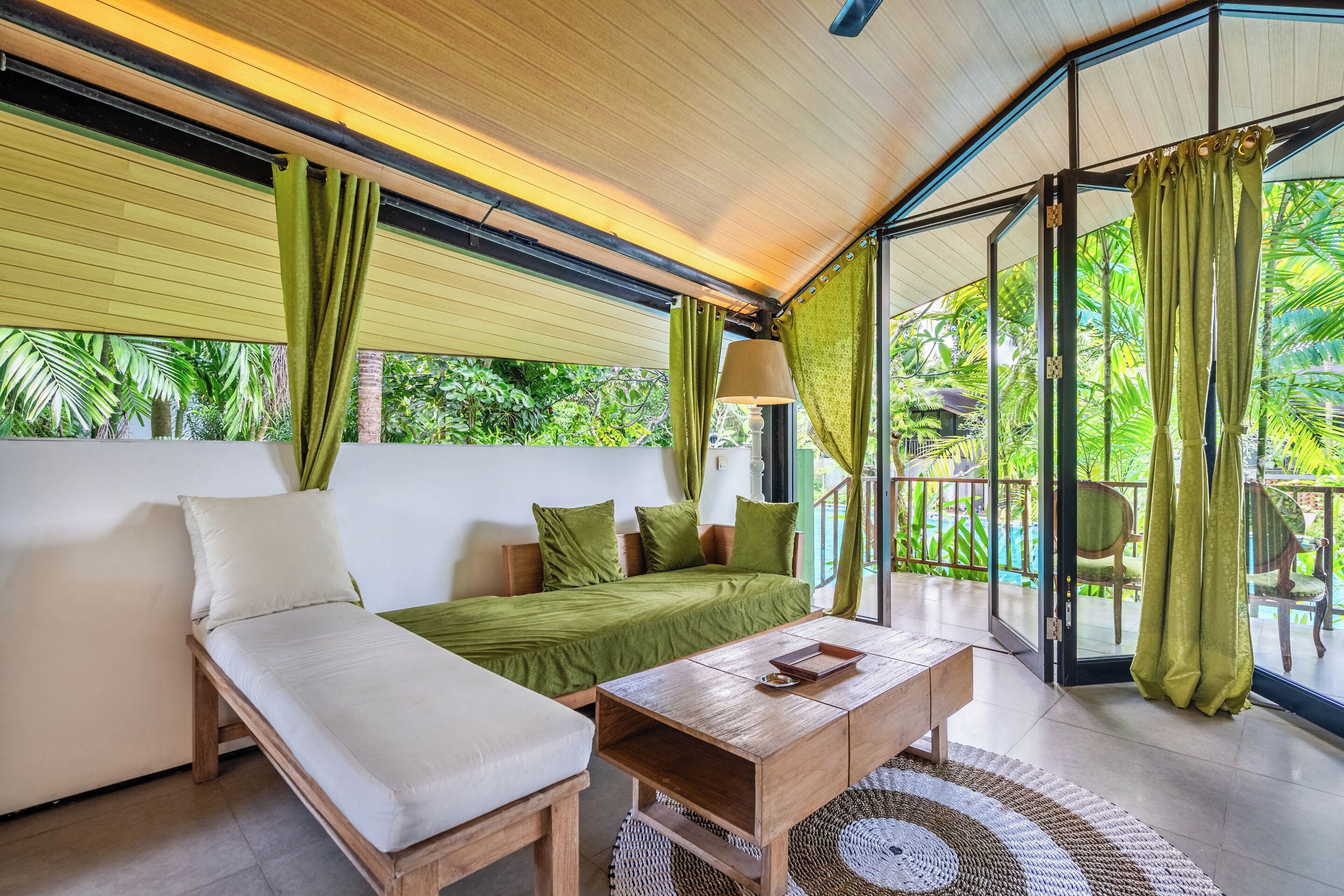 A room with a bed, a sofa, a wooden table, and a large window with curtains.