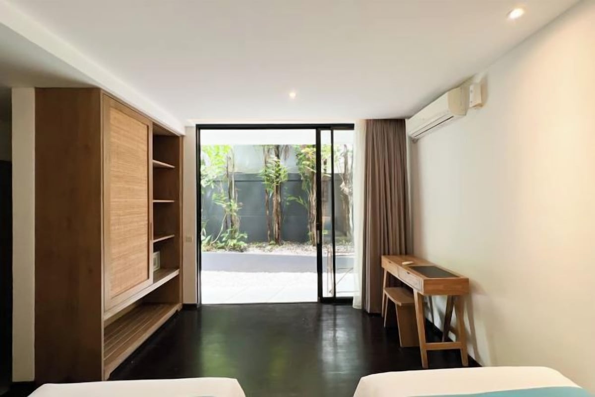 A hotel room with a sliding door leading to a balcony, a wooden wardrobe, and a small desk.