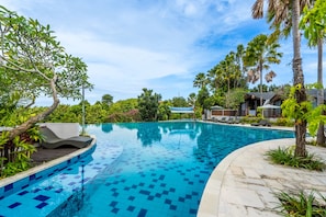 A swimming pool with tiled edges, lounge chairs, and a wooden deck. - Mana Villas Nusa Dua (Nusa Dua)