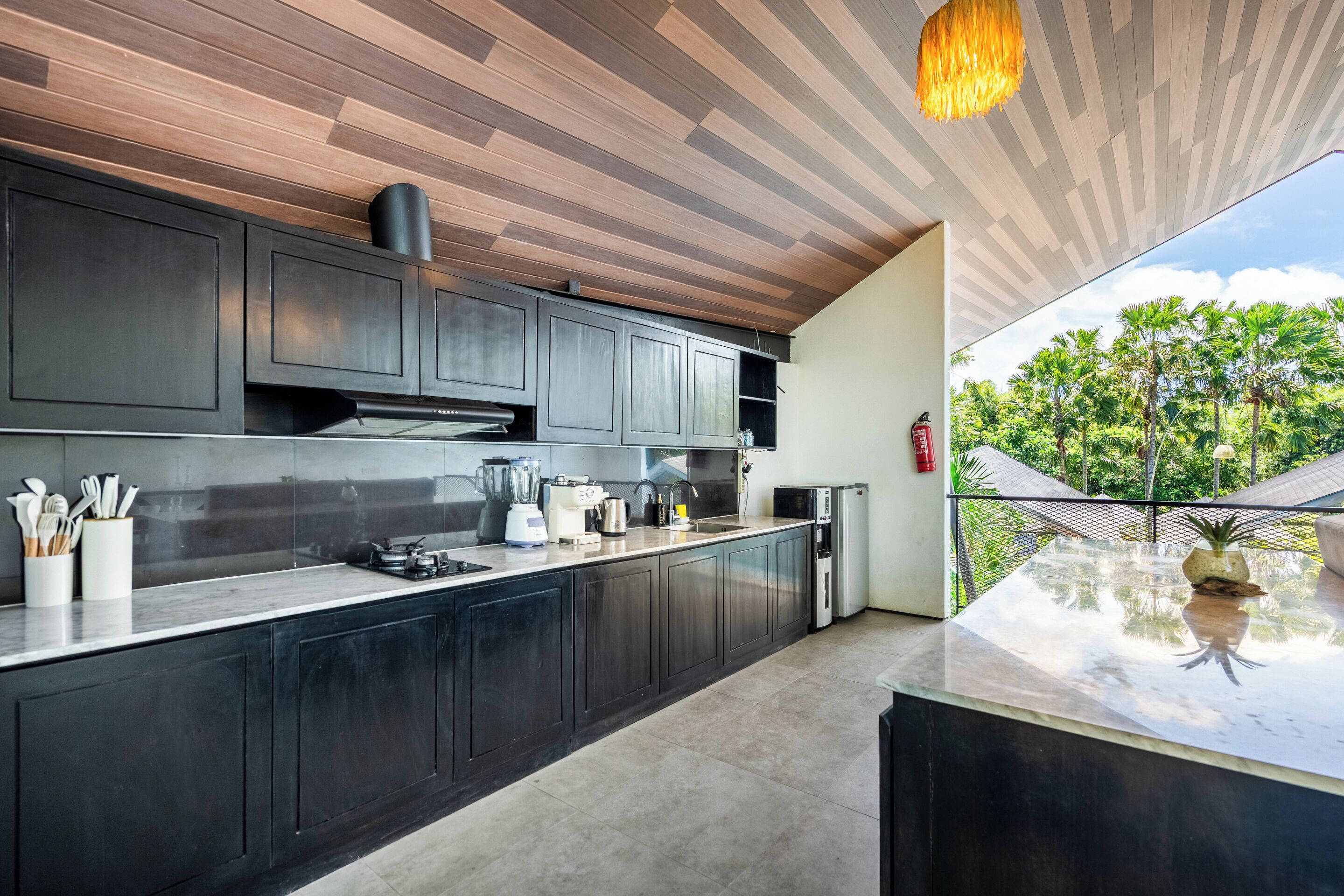 A modern kitchen with dark cabinetry, a countertop, and a view of greenery outside.