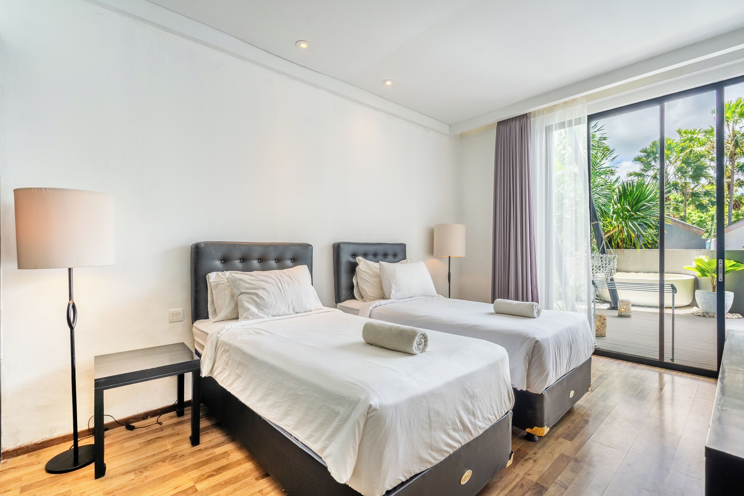 A hotel room with two beds, a large window, and a balcony with plants.
