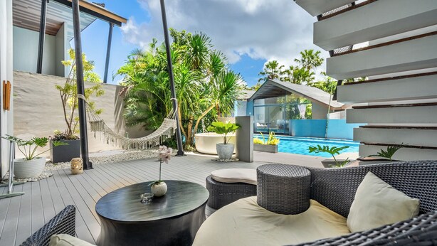 A modern outdoor patio with wicker furniture, a pool, and tropical plants. - Mana Villas Nusa Dua (Nusa Dua)