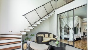 A modern interior with a staircase, wicker furniture, and a glass partition leading to a bedroom with a canopy bed. - Mana Villas Nusa Dua (Nusa Dua)
