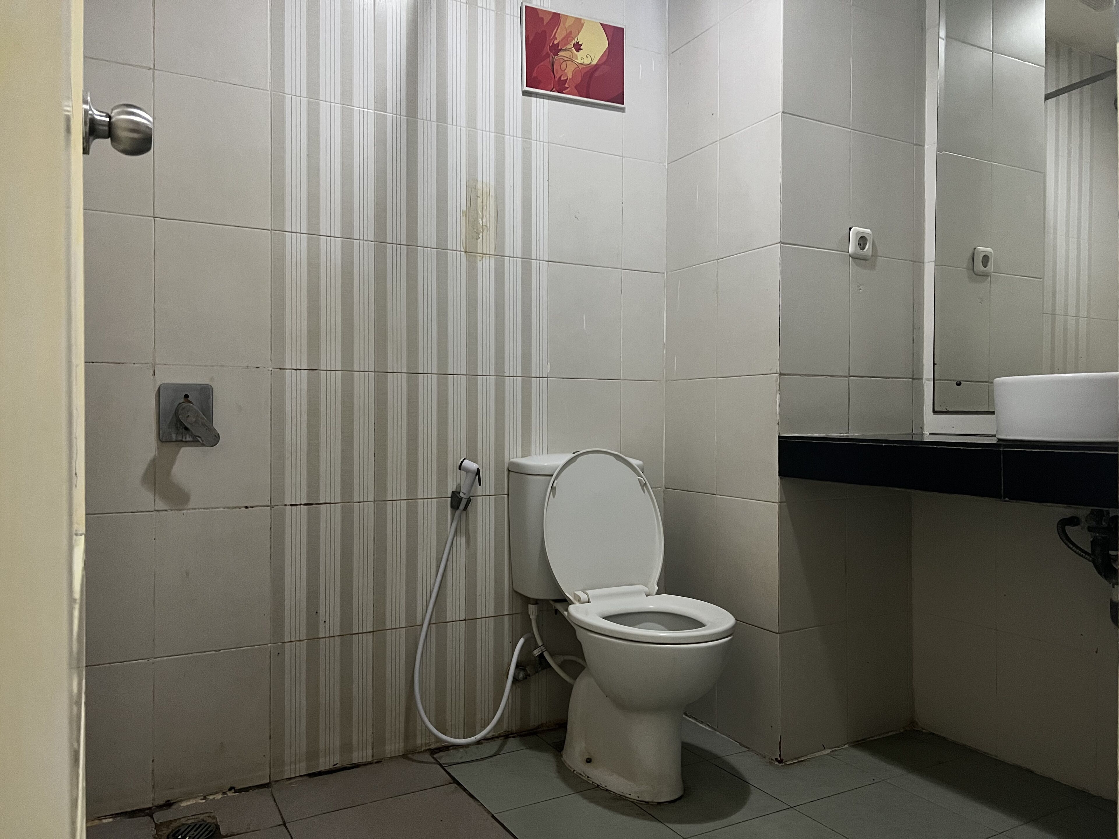 A small, basic bathroom with a toilet, a hand dryer, and a mirror.