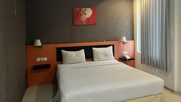 Quarto de hotel com uma cama grande, duas mesas de cabeceira com luminárias, ar condicionado fixado na parede, um quadro e uma janela com cortinas.