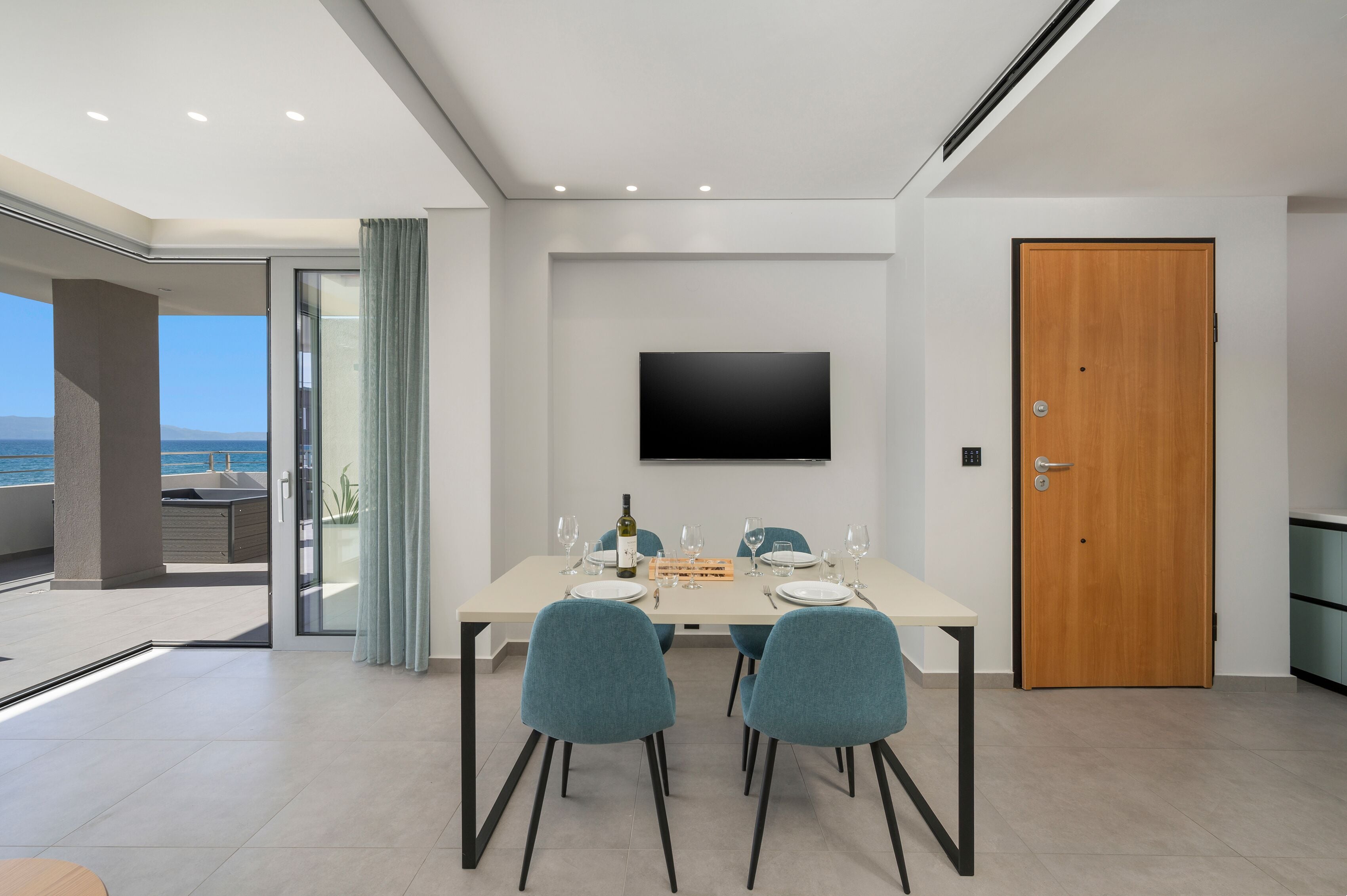 A modern dining area with a table set for two, a flat-screen TV mounted on the wall, and a wooden door.