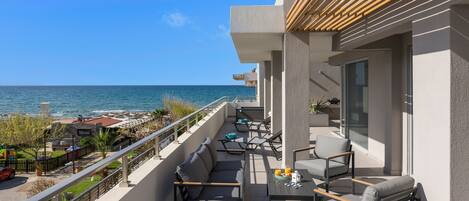 Uma varanda com área de estar externa, vista para o mar e um edifício com design moderno.