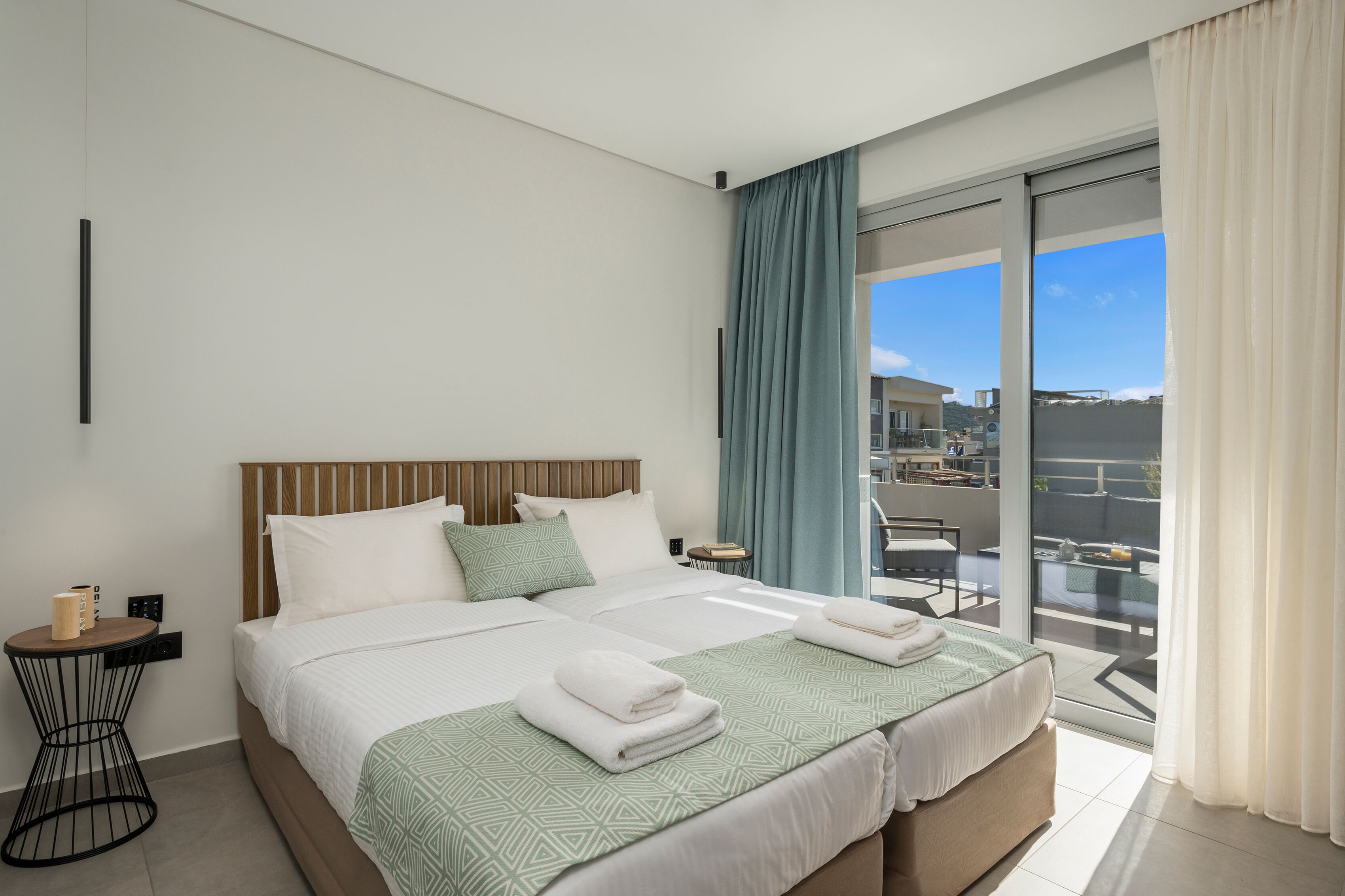 Een moderne hotelkamer met een groot bed, een klein nachtkastje en uitzicht op de stad vanaf het balkon.