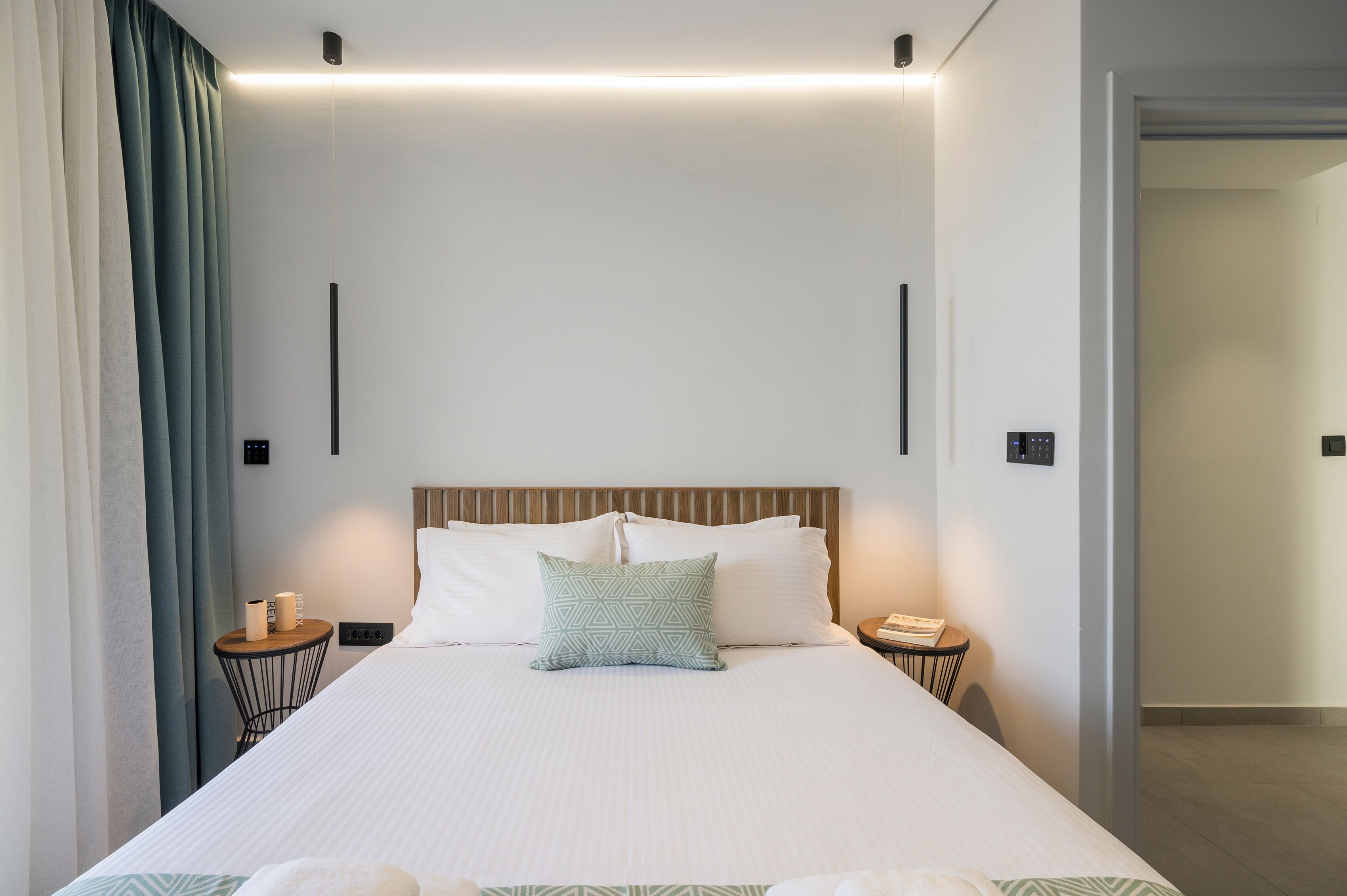 Una habitación de hotel moderna con una cama grande, una mesita de noche con lámpara y una lámpara de pared.