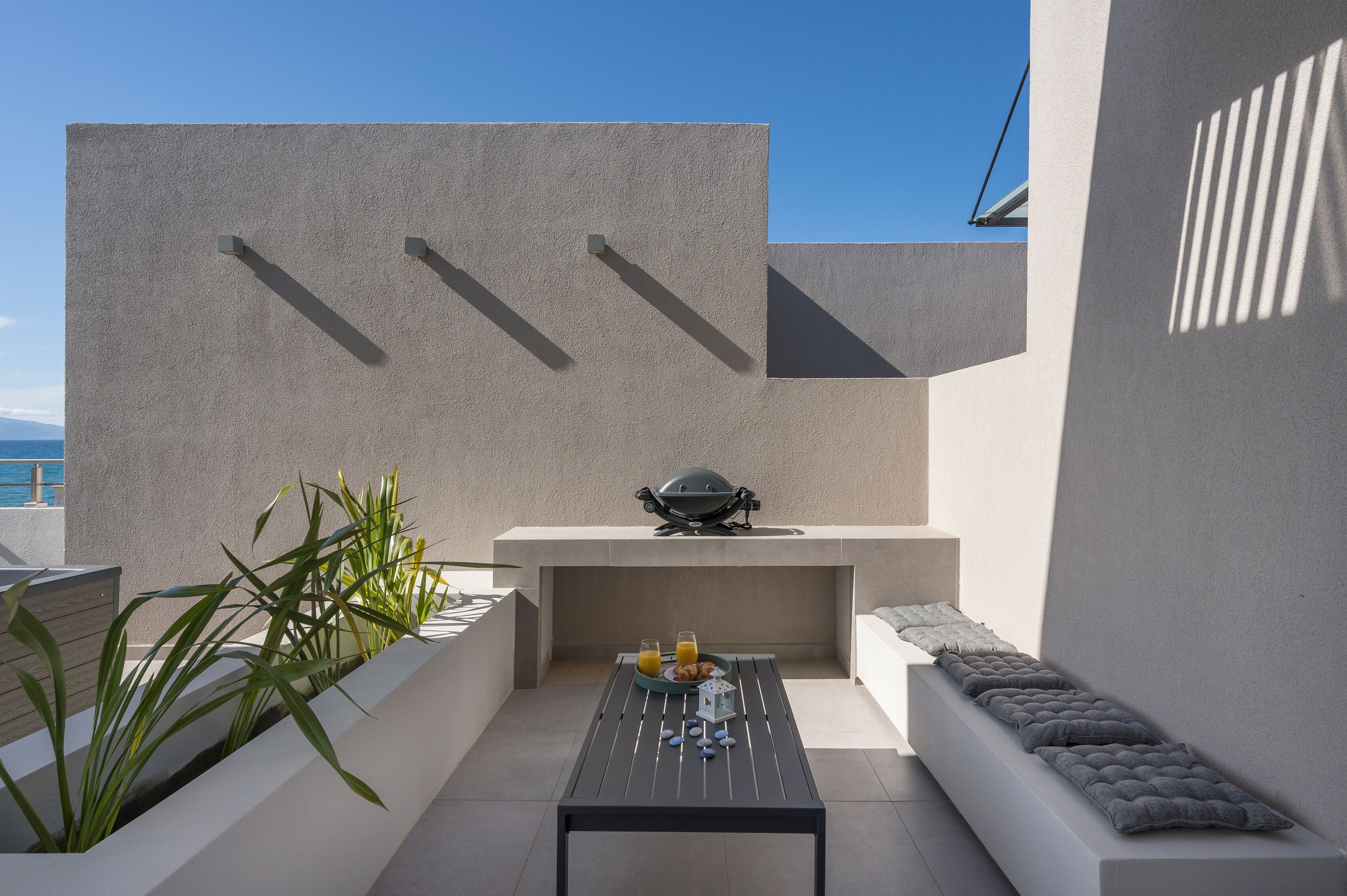 A modern outdoor seating area with a table, cushions, and a grill.