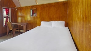 A bedroom with a wooden wall, a bed with white linens, a wooden chair, and a small table. - OYO 92419 Rejeng Homestay Near Kerta Gangga Waterfall (Gangga)