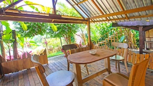 An outdoor wooden deck with a table and chairs, surrounded by lush greenery. - OYO 92419 Rejeng Homestay Near Kerta Gangga Waterfall (Gangga)