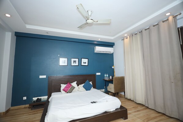 Une chambre à coucher comprenant un lit, un ventilateur de plafond, un appareil de climatisation, une table de chevet, une chaise et une fenêtre avec des rideaux.