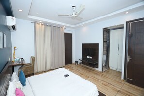 Une chambre d’hôtel comprenant un lit, une télévision, un ventilateur de plafond, un appareil de climatisation, un bureau avec une lampe et une porte donnant sur une autre pièce.