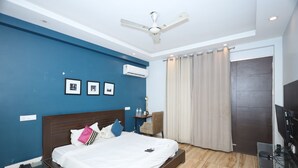 A bedroom with a bed, a ceiling fan, an air conditioning unit, a TV, and a door with curtains. - Wedlock Hotels (Gurugram)