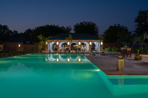 A swimming pool with a covered seating area and lounge chairs. - Aangan Resort Ranthambore  (Sawai Madhopur)