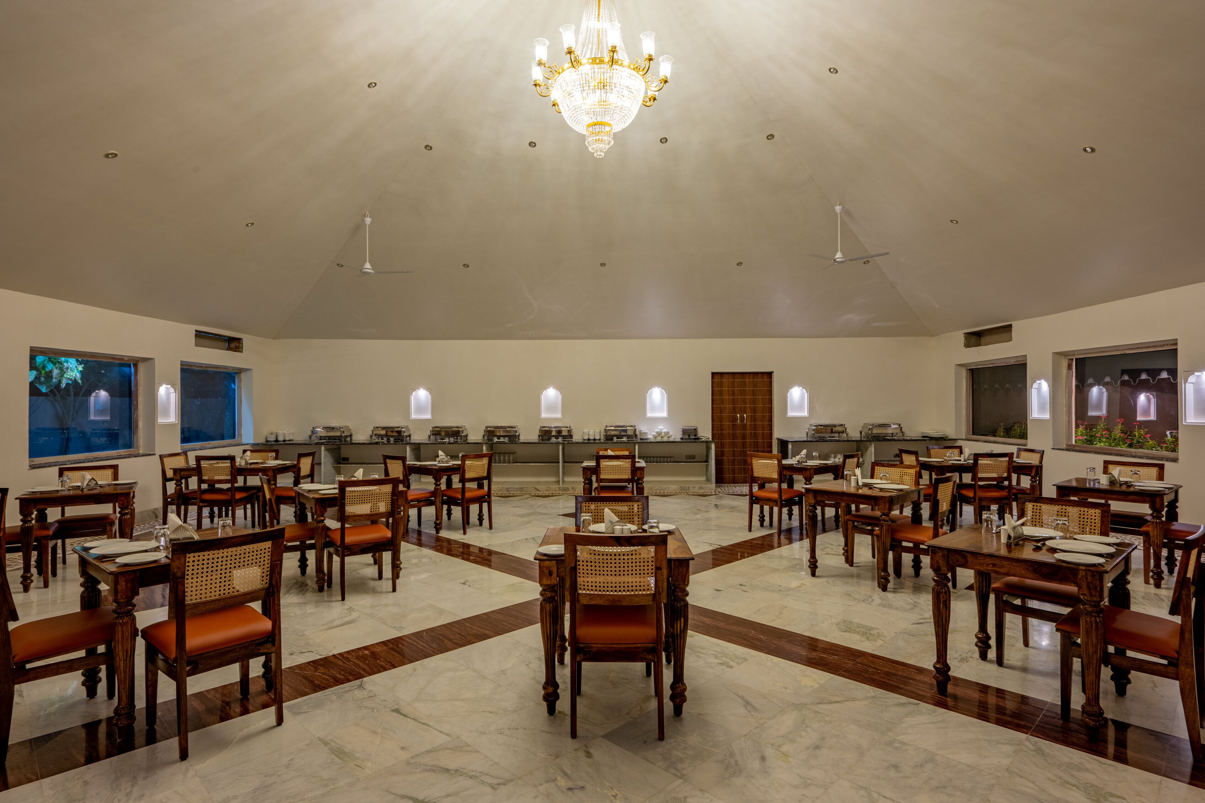 A spacious dining area with wooden tables and chairs, a chandelier, and large windows.
