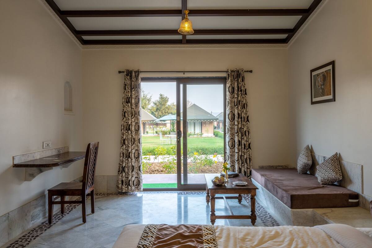 Ein Zimmer mit einem Bett, einem Schreibtisch, einem Stuhl, einer Bank und Blick ins Freie.
