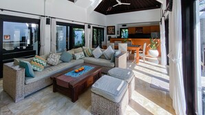 A spacious living area with a sofa set, a coffee table, and a dining table. There is a kitchen area visible in the background. - Cempaka Villa by Premier Hospitality (Nusa Dua)