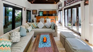A spacious living area with a sofa set, a coffee table with a decorative centerpiece, and a kitchen in the background. - Cempaka Villa by Premier Hospitality (Nusa Dua)