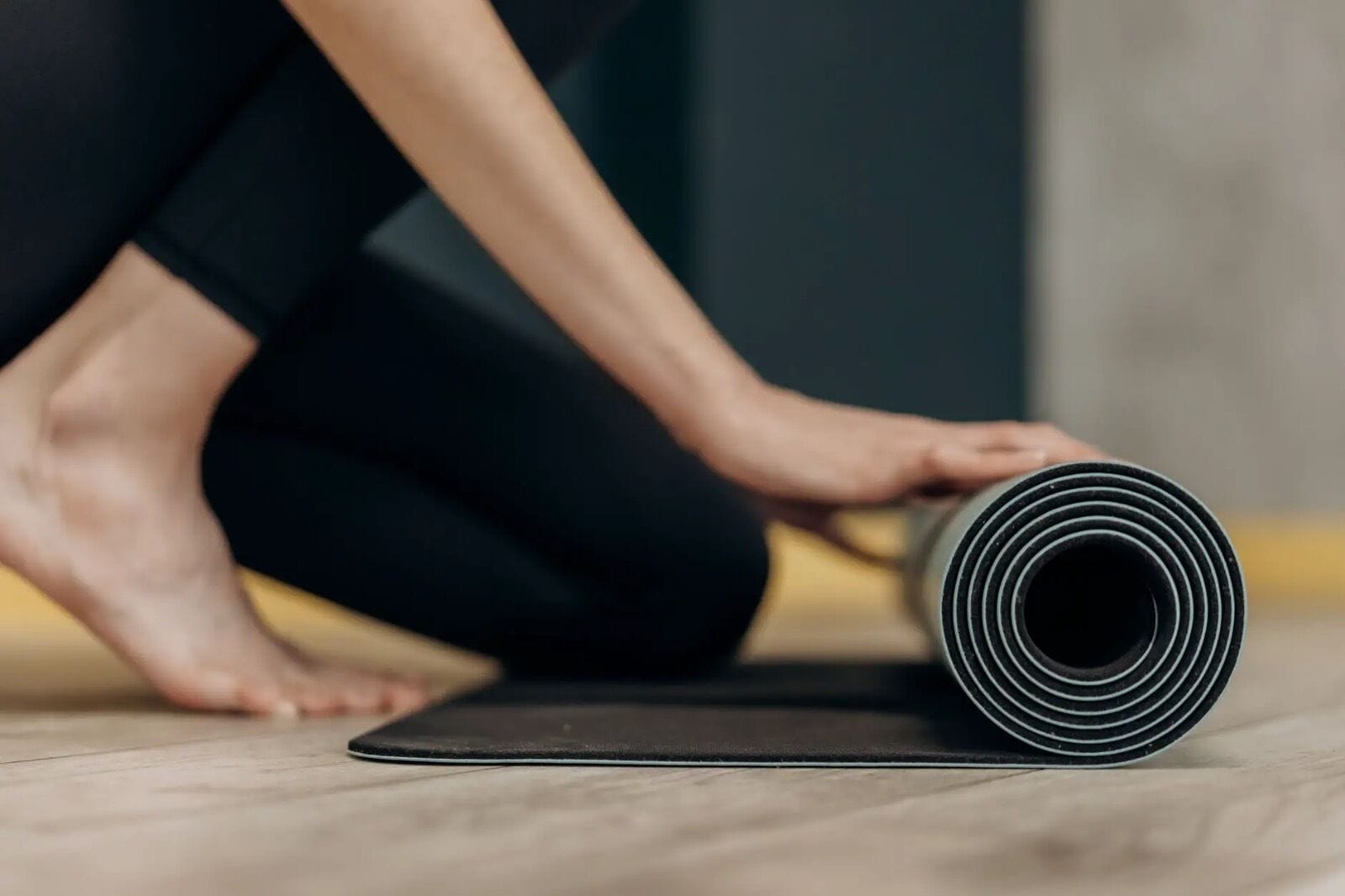 Una persona extiende una colchoneta de yoga negra sobre un suelo de madera.