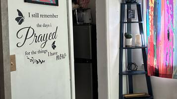 A room with a wall decal featuring a quote, a framed picture, a shelf with decorative items, and a colorful curtain.