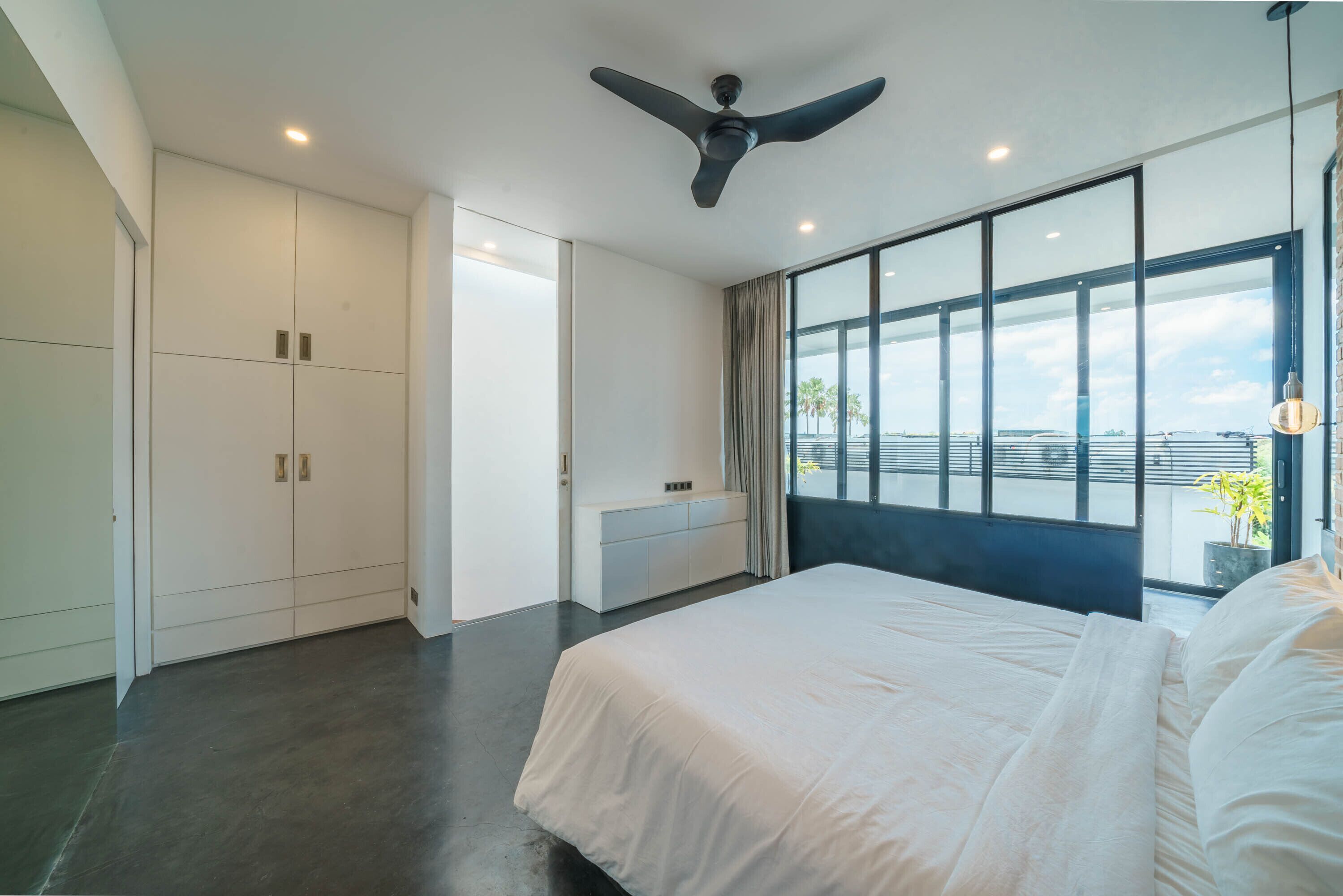 A modern bedroom with a large bed, a ceiling fan, a window with a view, and a wardrobe.