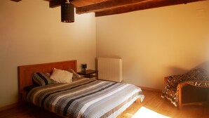 Ein Schlafzimmer mit Holzboden, einem Bett mit gestreifter Bettdecke, einem Nachttisch mit Lampe und einem Heizkörper.