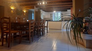 Ein Essbereich mit Holzbänken und einem Tisch, eine Küche mit weißen Schränken sowie eine Steinwand.