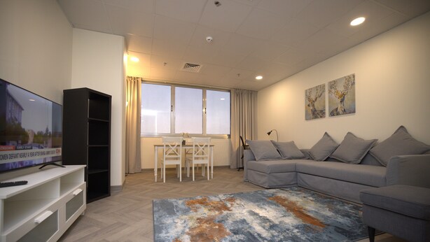 Un salon moderne avec un canapé gris, un téléviseur à écran plat, un meuble de rangement blanc, une table à manger avec des chaises et un grand tapis.