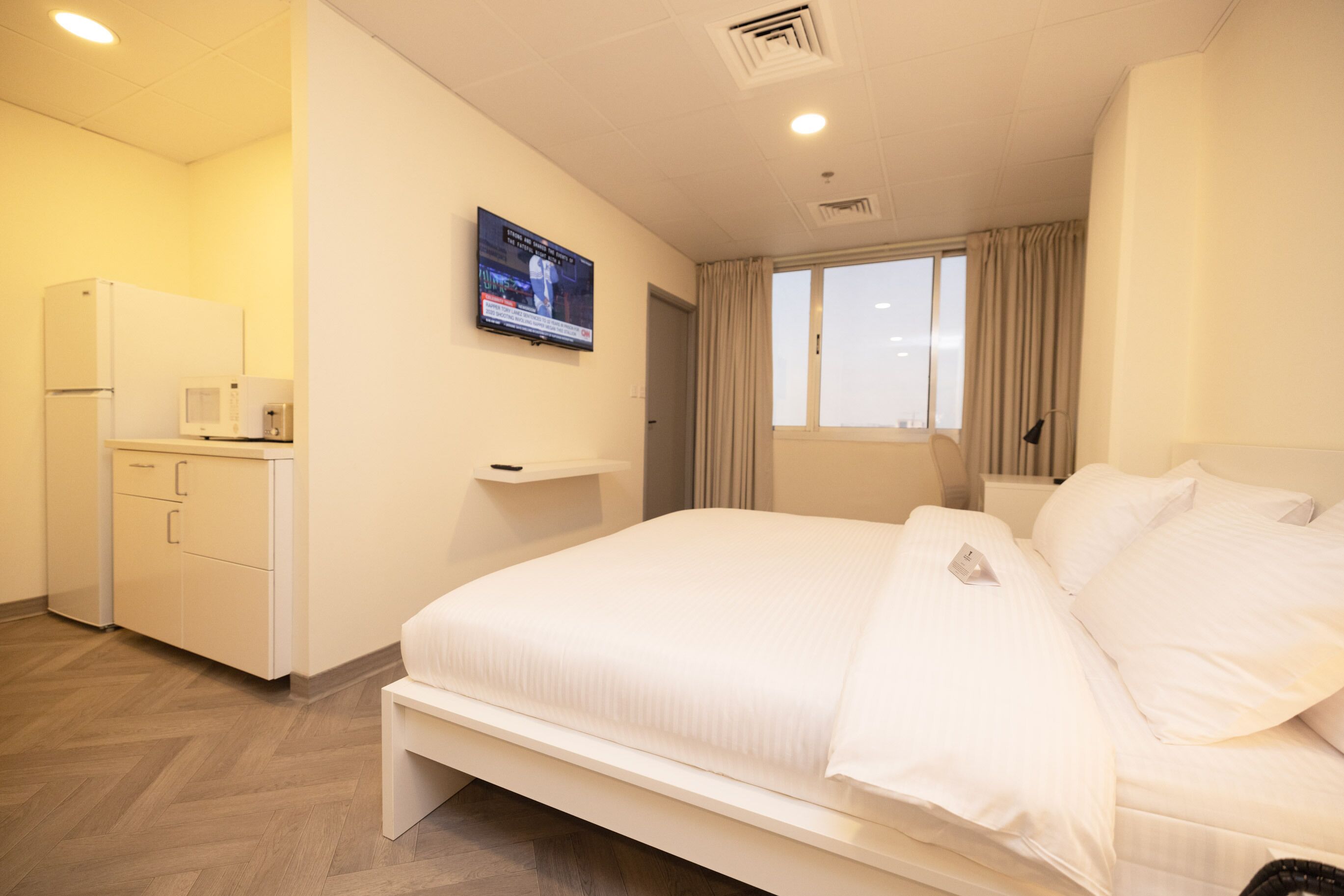 A hotel room with a bed, a television on the wall, a desk with a microwave, and a refrigerator.