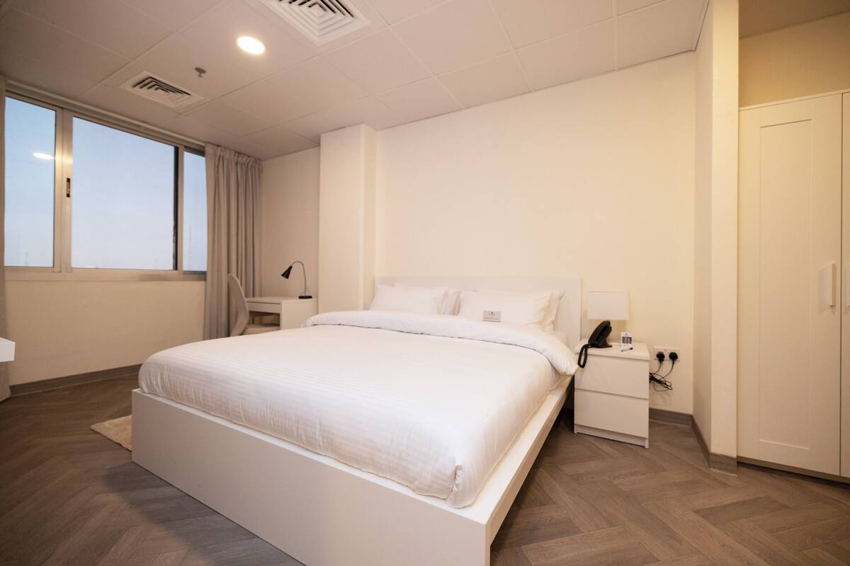Una habitación de hotel moderna con una cama grande, una mesita de noche y un armario.