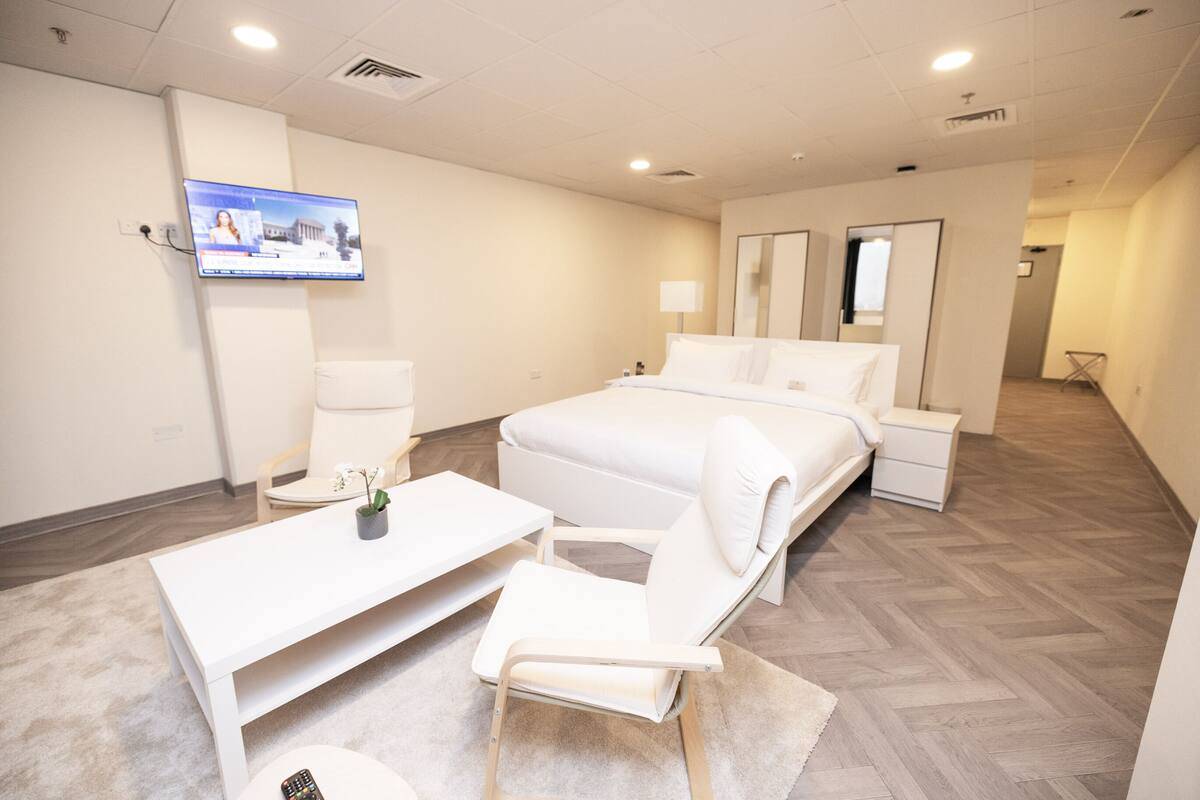 Habitación de hotel con cama, escritorio, silla, televisor montado en la pared y espejo.
