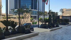Un bâtiment moderne, orné de plusieurs drapeaux, dont celui des Émirats arabes unis, et doté d’une zone pavée avec des jardinières et une clôture.