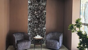 Un hall d’entrée avec deux fauteuils, une petite table ronde, un mur en marbre et une plante en pot.