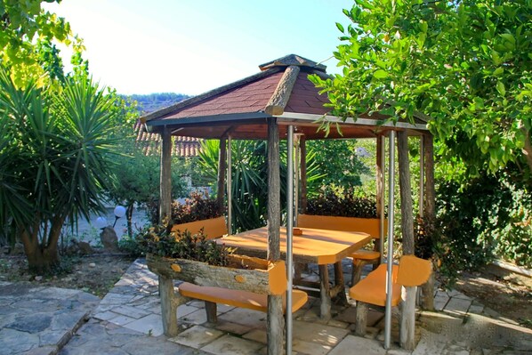 A wooden gazebo with a tiled roof, surrounded by lush greenery and stone pathways. - Private property with outdoor pool , cosy spaces and beautiful garden (Kato Archanes)