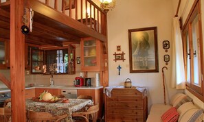 Una habitación acogedora con una escalera de madera, una mesa de comedor con mantel estampado, un aparador de madera y una cama con almohadones a rayas.